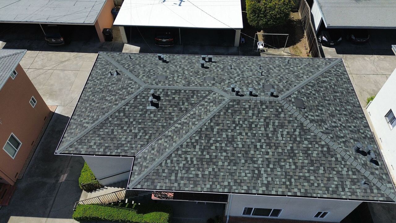Wider aerial showing the finished Landmark shingle roof with adjacent carports and neighboring single-ply flat roofs