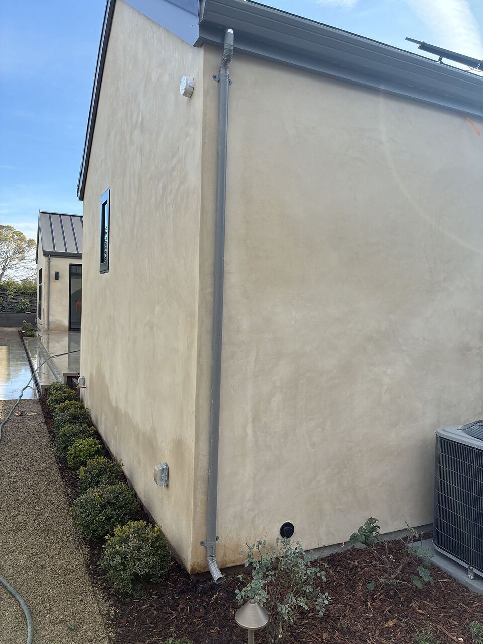 Full-run downspout against stucco wall running from eave to grade