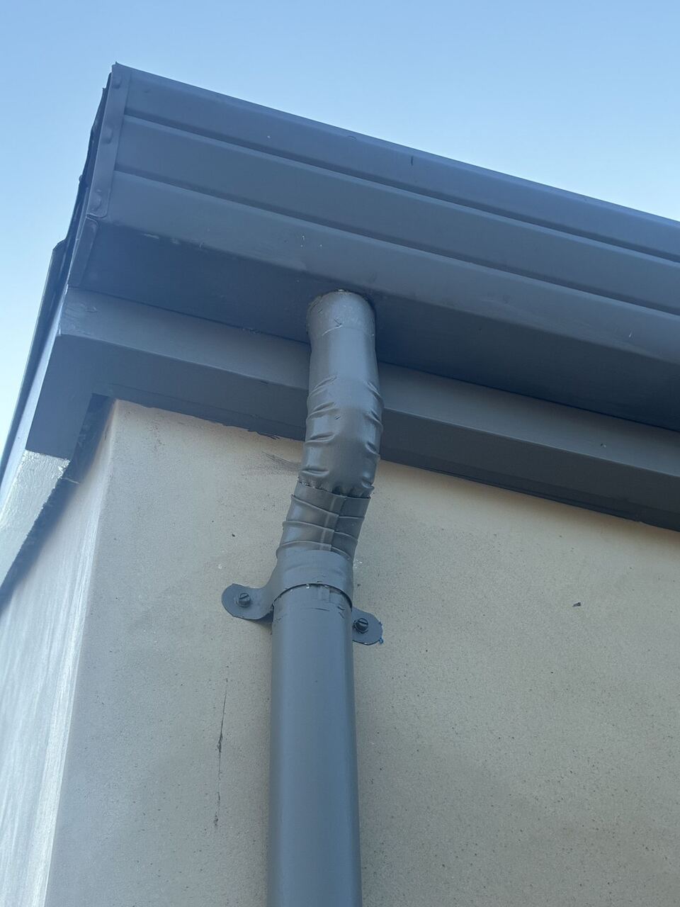 Gutter outlet transitioning to round downspout with color-matched strap hardware