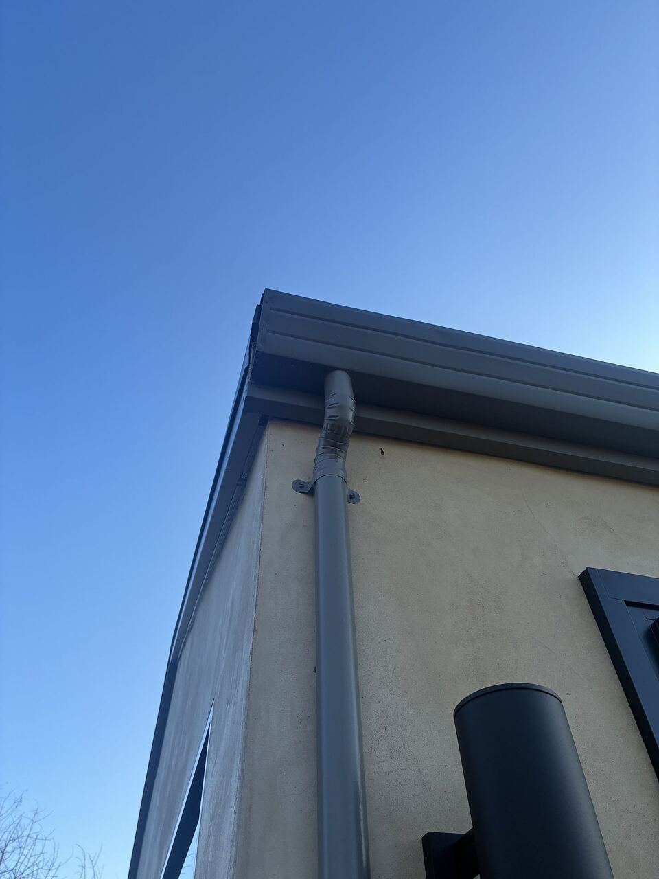 Outside corner detail of dark gray gutter with round downspout